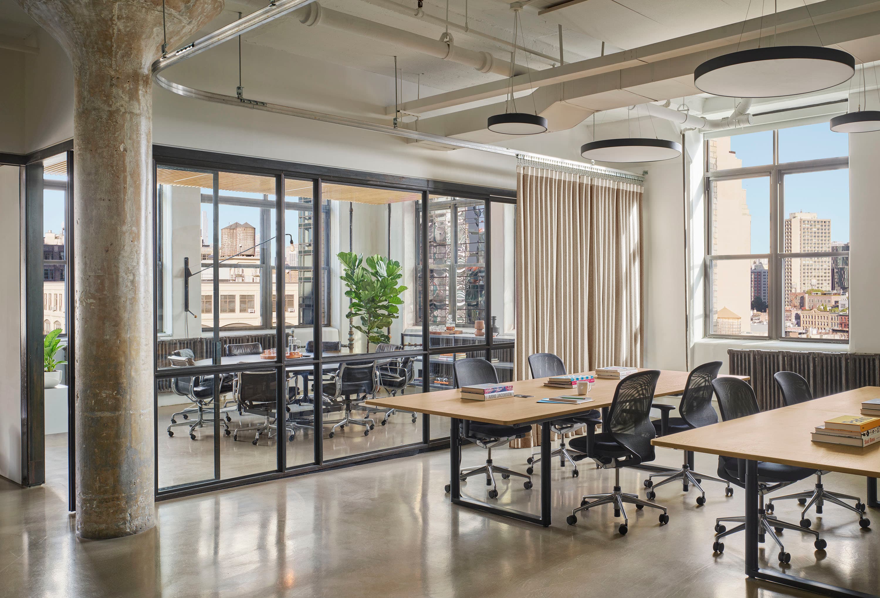 View of an enclosed glass office and two work desk stations with piles of books